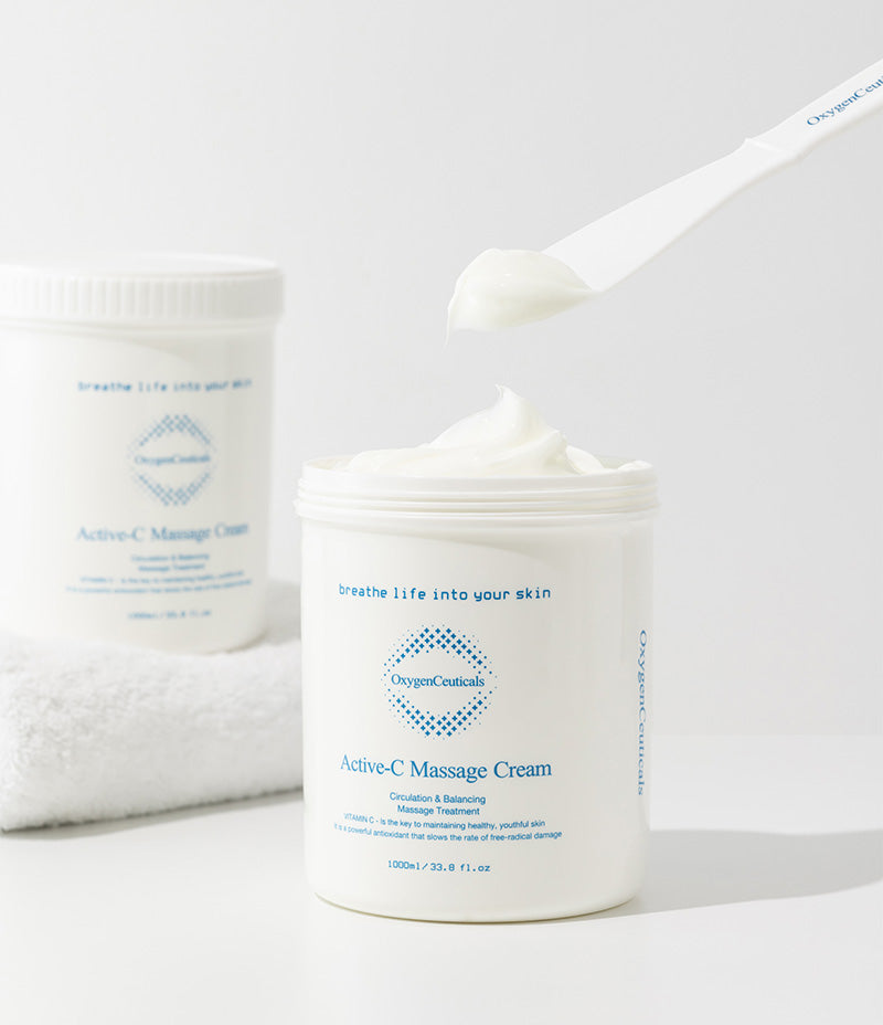 Active-C Massage Cream open jar with a spatula lifting a scoop of white cream; a second jar rests on a white towel behind