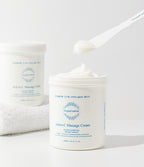 Active-C Massage Cream open jar with a spatula lifting a scoop of white cream; a second jar rests on a white towel behind