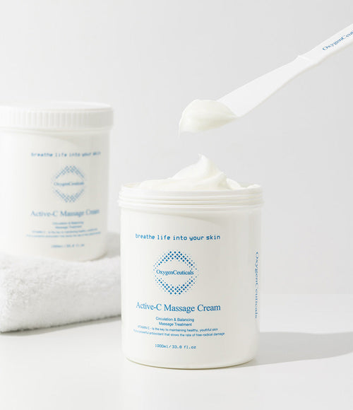Active-C Massage Cream 已開蓋的罐，白色匙形用具挑起一團乳霜；後方白色毛巾上放著另一罐